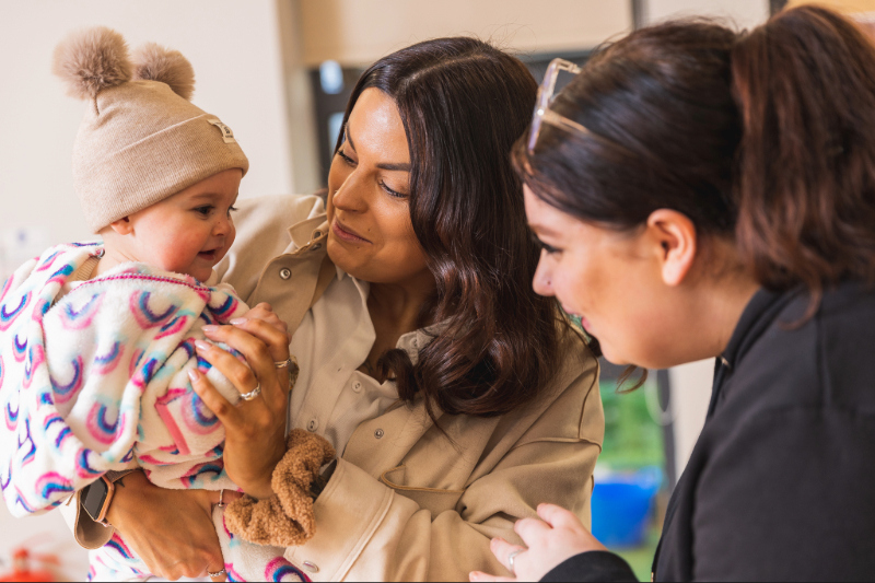 Nursery-parent-baby-key-worker Practitioner welcoming family to nursery